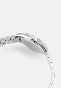Montre argentée avec un bracelet en acier inoxydable, boîtier rond et un cadran noir avec des accents dorés. Comprend une couronne surélevée et une texture lisse.