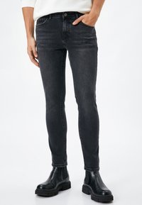 Jeans negros ajustados para hombre, hechos de denim, con bolsillos frontales, pasadores para cinturón y un ligero desgaste, combinados con botas negras hasta el tobillo.