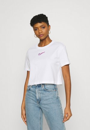 T-shirt bianca in cotone tagliata, con logo Nike viola sul petto. Abbinata a jeans di denim azzurri a vita alta.