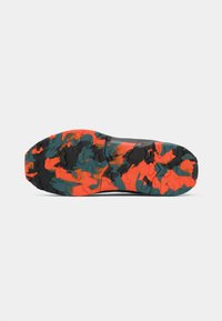 Sola de sapato com um padrão texturizado em preto, laranja brilhante e cores de camuflagem verde escuro sobre um fundo branco.