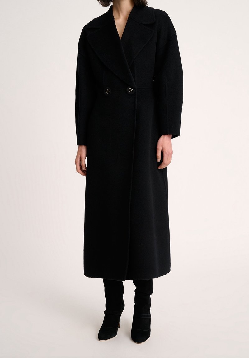 Czarny wełniany płaszcz o kroju dwurzędowym, z dużymi klapami i długimi rękawami, ozdobiony dekoracyjnymi guzikami, o prostym kroju sięgającym kostek.