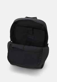 Sac à dos noir avec un dessus zippé, en matière textile, poche intérieure et poche à rabat à l'avant. Fini mat, design simple, sans motifs visibles.