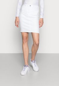Witte denim rok met een getailleerde silhouet, voorzien van een vijf-pocket ontwerp en een sluiting met een frontknop. Gecombineerd met witte sneakers.