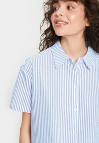 Camicia a strisce maniche corte in cotone blu chiaro e bianco, con colletto e bottoni sul davanti. Tessuto morbido e vestibilità casual.