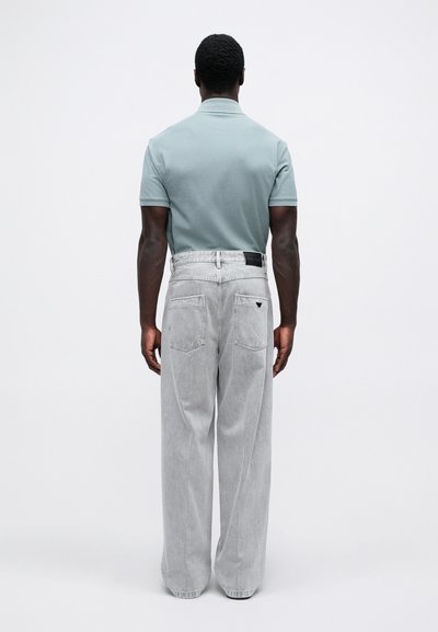 Grå denim vide bukser med to baglommer, sort label, parret med en lyseblå kortærmet polo-shirt. Neutral baggrund.