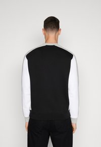 Felpa in cotone con collo rotondo, caratterizzata da blocchi di colore nero, bianco e grigio, con polsini e orlo a costine, e una texture liscia.