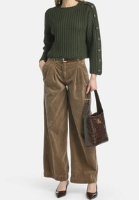 Ciemnozielony prążkowany sweter z bocznym detalem na guziki, beżowe szerokie spodnie z sztruksu, brązowa torba z tłoczeniem imitującym skórę krokodyla, czarne spiczaste buty.