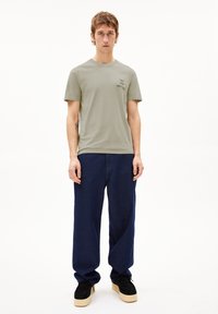 Groene katoenen T-shirt met korte mouwen en een bedrukt tekstlogo op de borst, gecombineerd met losse donkerblauwe spijkerbroeken en zwarte schoenen.