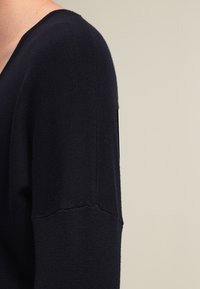 Pull en tricot bleu marine avec un décolleté en V profond et des manches longues. Se distingue par une finition texturée et une couture visible à l'épaule.