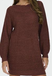 Abito maglione chunky di colore ruggine profondo con scollatura ampia, maniche lunghe e texture a costine. L'orlo è leggermente sopra metà coscia.