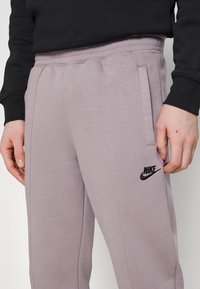 Pantalones de chándal de algodón gris claro con bolsillos laterales, cinturilla elástica y logotipo negro de Nike en la pierna izquierda. Textura suave y corte recto.
