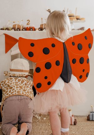 Alas de mariquita en rojo brillante con manchas negras, hechas de tela. Combínalas con una blusa blanca y una falda de tul rosa esponjosa, creando un disfraz divertido.
