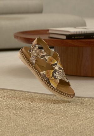 Καφέ και κίτρινα σανδάλια με σχέδιο φιδιού, με λουριά που διασταυρώνονται, σόλα τυλιγμένη με τζούτ και διχτυωτό δερμάτινο πέλμα.