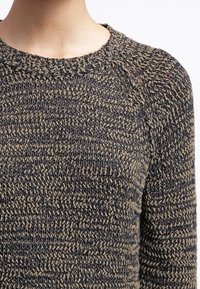 Stickad tröja med en melerad mörkblå och beige mönster, rund halsringning och en texturerad yta som ger en mysig känsla.