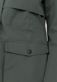 Giacca verde con una grande tasca a pattina e chiusura a scatto nera. Il tessuto è liscio, con una sottile texture e linee di design eleganti.