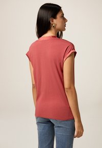 T-shirt a maniche corte, collo rotondo di colore rosa, realizzato in tessuto morbido. Presenta maniche arrotolate e una vestibilità rilassata.