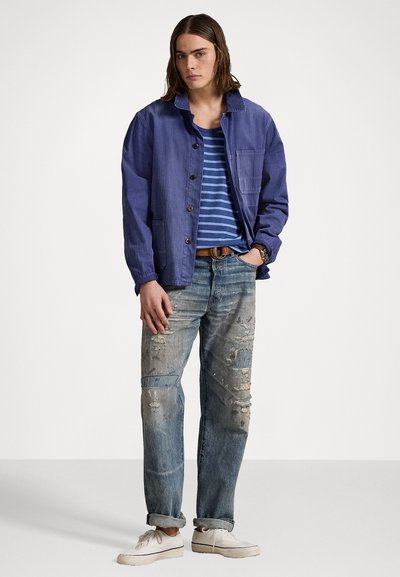 Blå denimjacka med knappar, randig blå och vit t-shirt, slitna blå jeans och vita sneakers. Avslappnad passform och stil.