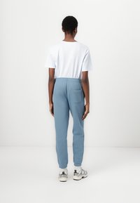 Lys blå joggebukser med elastisk liv, sidelomme og ribbede mansjetter, parret med en enkel hvit t-skjorte. Enkel design.