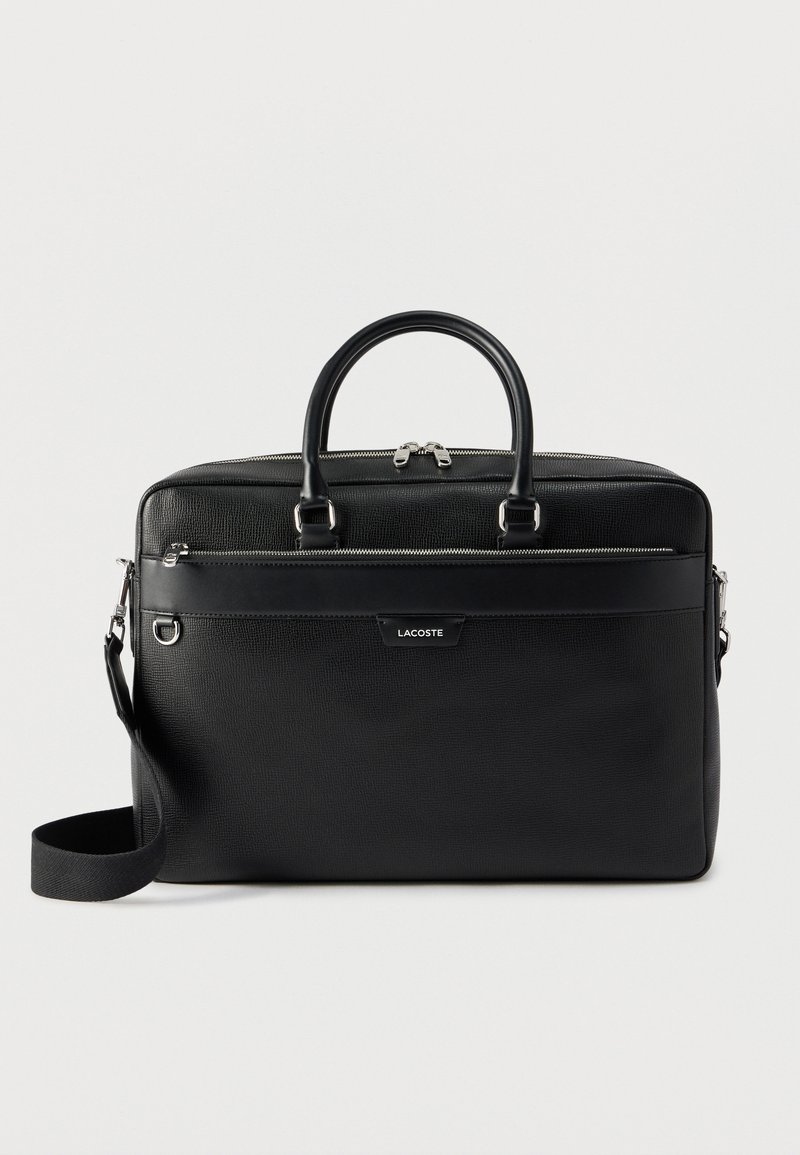 Mallette en cuir noir texturé avec deux poignées, bandoulière amovible, poche avant zippée et ferrures argentées.