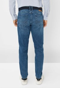 Jeans in denim blu con taglio dritto, dotati di due tasche posteriori e una cintura intrecciata blu navy. Il tessuto presenta una leggera trama e una finitura sbiadita.