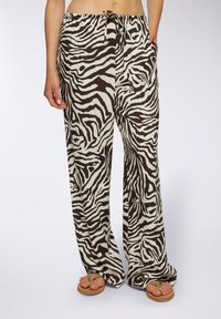 Pantaloni a gamba larga in un tessuto beige con un motivo a strisce zebra nere. Presentano una vita elastica con cordino e tasche laterali.