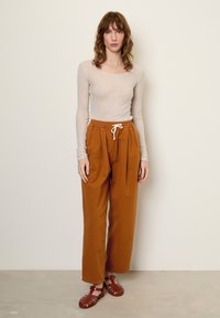 Svetlo šedý dlhý rukáv, voľný strih, spojený s terakotovými širokými nohavicami s elastickým pásom a šnúrkou. Hnedé sandále.