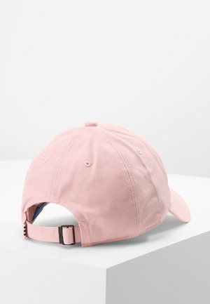 Gorra de béisbol de algodón color rosa claro con correa de tela ajustable y hebilla metálica, vista desde atrás, reposando sobre una superficie blanca.