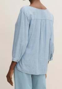 Blusa a strisce blu chiaro con maniche a tre quarti, scollo rotondo e vestibilità comoda. Tessuto morbido con una lieve texture.