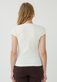 Top corto bianco, strutturato, con maniche corte, dalla forma aderente e scollatura rotonda, abbinato a pantaloni marroni. Il tessuto presenta una leggera rigatura orizzontale.