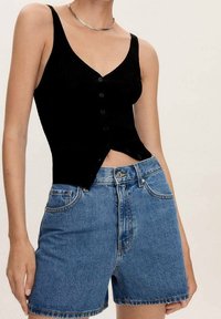 Top sin mangas negro con canalé, escote en V y botones en el frente, combinado con shorts de mezclilla azul claro con un diseño estándar de cinco bolsillos.