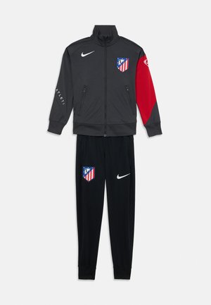 Survêtement Nike en gris foncé et rouge, comprenant une veste zippée avec un logo et un pantalon noir assorti avec le logo sur le côté. Fabriqué en tissu lisse.