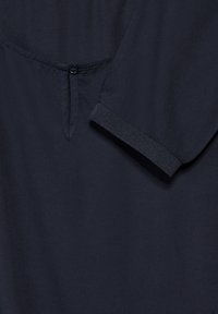 Marineknappet skjorte detalje med synlig knap, diskret krave og tekstureret manchet. Glat stof med et enkelt design.