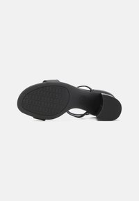 Sandal con tacco nero e suola in gomma testurizzata, a punta aperta e con cinturini sottili. Il tacco presenta una leggera curvatura, che offre stabilità.