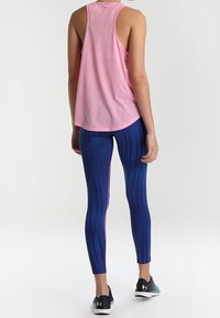 Rosa ärmlös topp som kombineras med blå mönstrade leggings med rosa sidestreck, bärs med svarta träningsskor. Slät tygtextur.