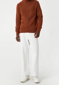 Suéter de punto color óxido con cuello alto, combinado con jeans blancos de pierna ancha y zapatillas blancas. El suéter tiene puños y dobladillo acanalados.