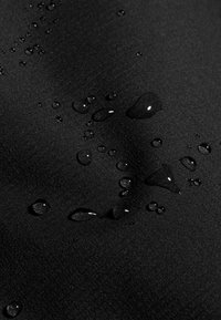 Des gouttes d'eau perlent sur un tissu noir lisse, montrant une texture de surface résistante à l'eau.