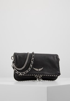 Schwarze Lederhandtasche mit silberner Kettenriemen, genieteten Kanten und einem flügelförmigen Metallemblem auf der vorderen Klappe, liegend auf einer weißen Oberfläche.