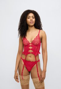 Σετ ε σωρούχων από κόκκινη δαντέλα με σουτιέν plunge που έχει λεπτομέρειες από λουλουδένια δαντέλα και ζώνη ζαρτιέρας, συνδυασμένο με ταίριαστα εσώρουχα και κάλτσες δαντέλας.