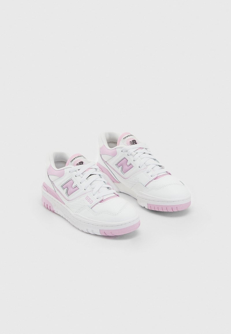 Paire de baskets New Balance blanches et rose clair avec lacets, logo sur le côté et semelles texturées, présentée sur fond uni.