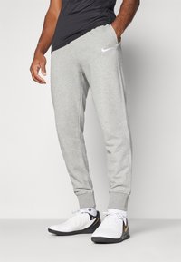 Pantaloni felpa grigi in cotone con vestibilità afusolata, caratterizzati dal logo Nike bianco, tasche laterali e polsini a coste. Abbinati a scarpe da ginnastica bianche.