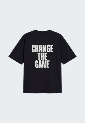 Zwart T-shirt met korte mouwen met daarop in het wit een gedurfde tekst "CHANGE THE GAME" gecentreerd op de achterkant tegen een effen achtergrond.