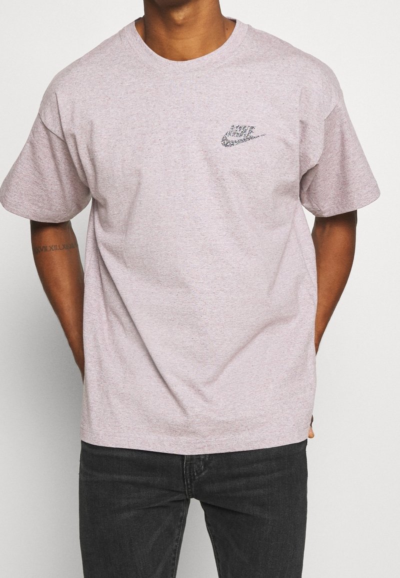 Světle růžové tričko vyrobené z bavlny, s krátkými rukávy a kulatým výstřihem, s černým logem Nike na levé části hrudi.