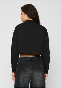 Svart kort genser med høy hals og lange ermer, kombinert med falmete svarte denimjeans med to baklommer og merkevare.