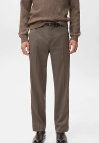 Pantalones marrones a medida, fabricados en tela suave, con corte de pierna recta, presillas para cinturón y pliegues frontales, combinados con botas negras.
