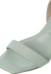 Sandale vert clair à bout ouvert avec une large bride frontale et un design à bout carré, montrant une partie de la semelle intérieure et extérieure.
