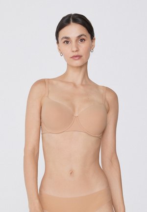 Soutien-gorge beige à décolleté plongeant avec des coques moulées et des bretelles réglables, fabriqué en tissu lisse. La conception avec armatures renforce le soutien et la forme.