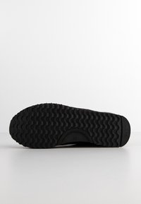 Czarna gumowa podeszwa buta z falistym bieżnikiem, rozmiar 37 oznaczony na środku, ułożona płasko na białej powierzchni na tle białego tła.