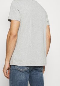 Camiseta de algodón gris de manga corta, con un corte relajado y un dobladillo recto, combinada con jeans de mezclilla azules con bolsillos traseros.
