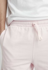 Pantalons de survêtement rose clair avec une taille élastique à cordon de serrage et des poches latérales. Fabriqués en tissu doux et lisse avec une coupe décontractée.