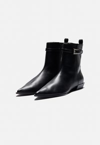 Bottines en cuir noir avec un bout pointu, une fermeture éclair sur le côté et une sangle dotée d'une boucle en argent. Texture lisse et talon bas.